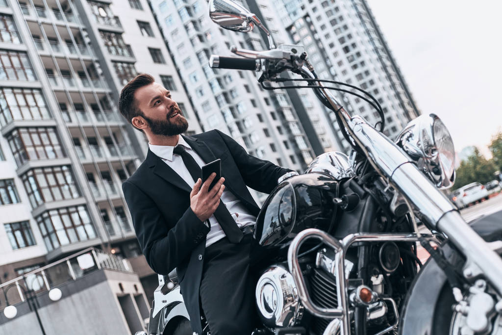 Módní obchodník drží chytrý telefon a sedí na motorce  - Fotografie, Obrázek