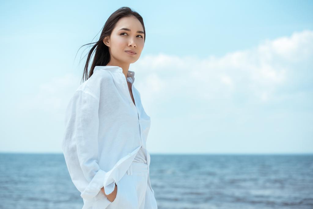 giovane donna asiatica con le mani in tasca guardando lontano dal mare
  - Foto, immagini