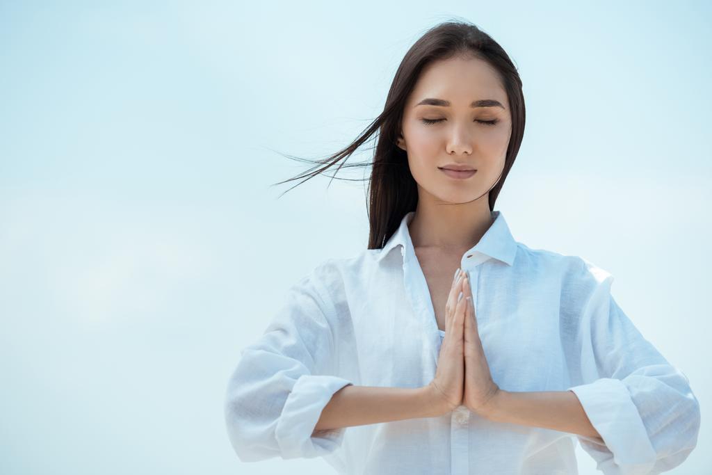 asian woman with closed eyes doing namaste mudra gesture against blue sky - Photo, Image