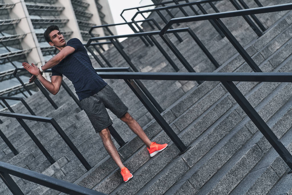 pleine longueur de l'homme en vêtements de sport étirant les mains sur les escaliers au stade
  - Photo, image