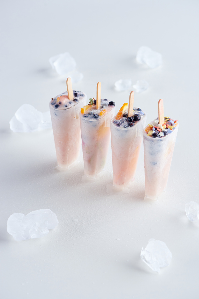 vista de ángulo alto de paletas dulces caseras con frutas y bayas y cubitos de hielo en gris
    - Foto, Imagen