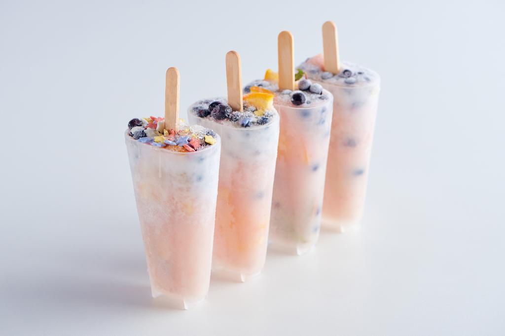zoete zelfgemaakte ijslollys met fruit en bessen in containers op grijs   - Foto, afbeelding