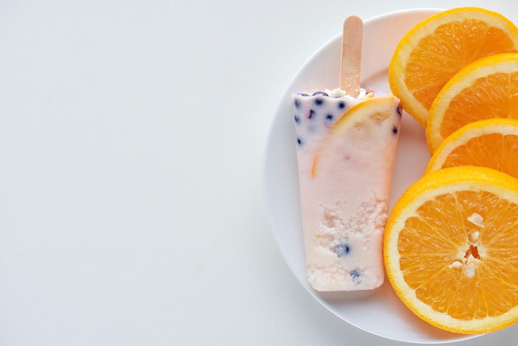 top view of delicious homemade popsicle with berries and slices of orange on plate on grey  - Photo, Image