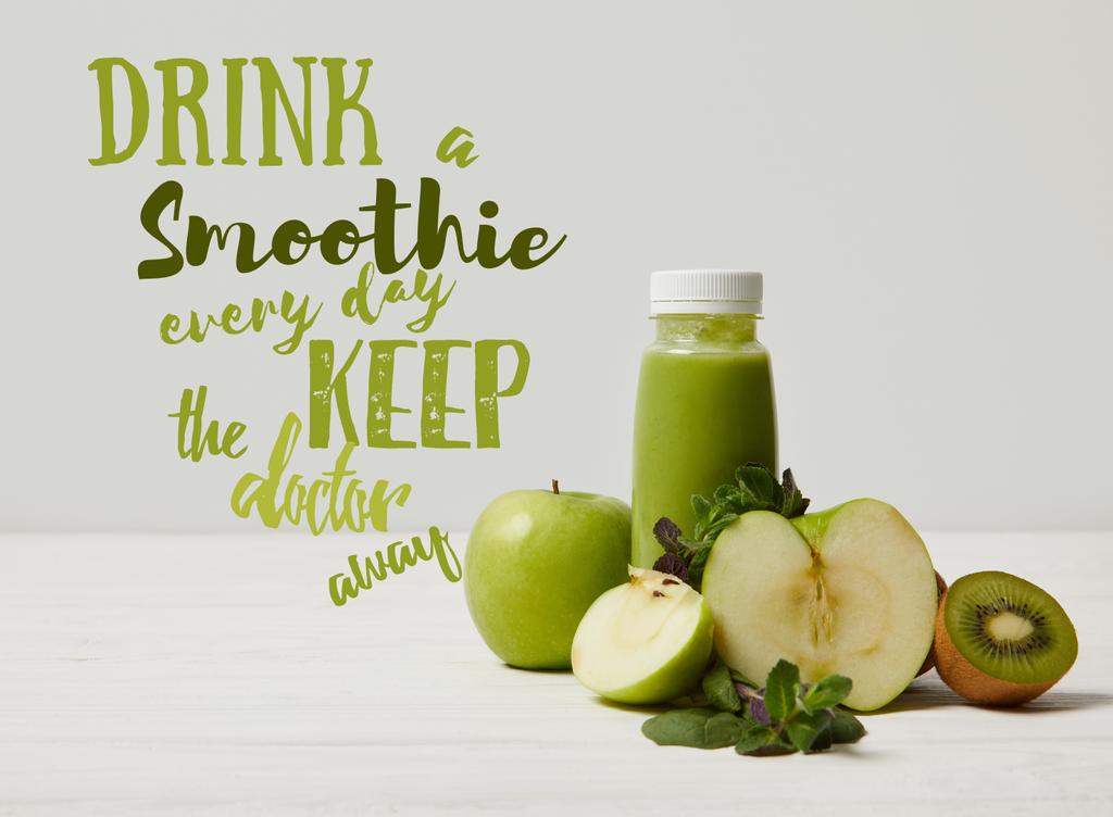 groene detox smoothie met appels, kiwi en mint en op witte houten oppervlak, drankje smoothie elke dag houd arts weg inscriptie - Foto, afbeelding