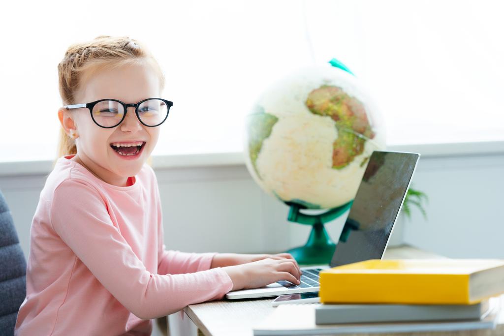 adorable écolière heureuse en lunettes étudiant avec ordinateur portable et livres à la maison
 - Photo, image