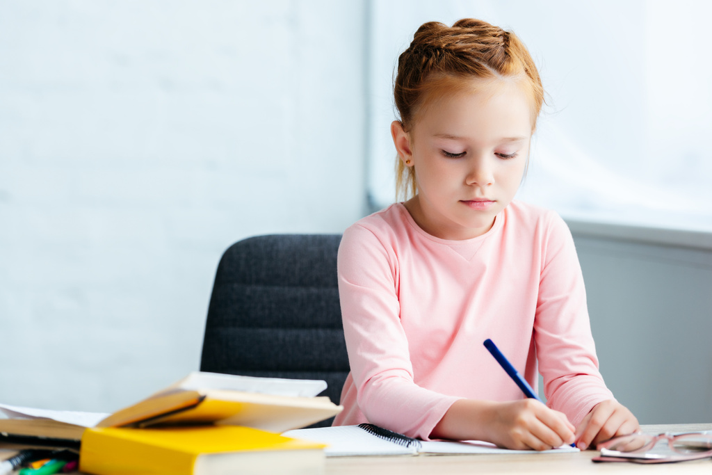 adorabile studentessa dai capelli rossi seduta alla scrivania e che studia a casa
  - Foto, immagini