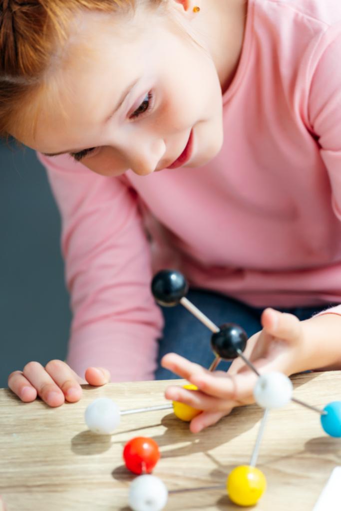 lähikuva söpö hymyilevä koulutyttö tarkastellaan molekyylimalli
 - Valokuva, kuva