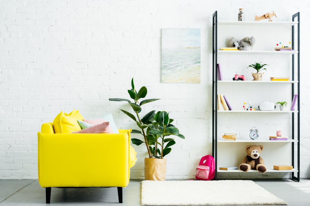 gemütliches Interieur mit gelber Couch und Büchern mit Spielzeug im Regal  - Foto, Bild