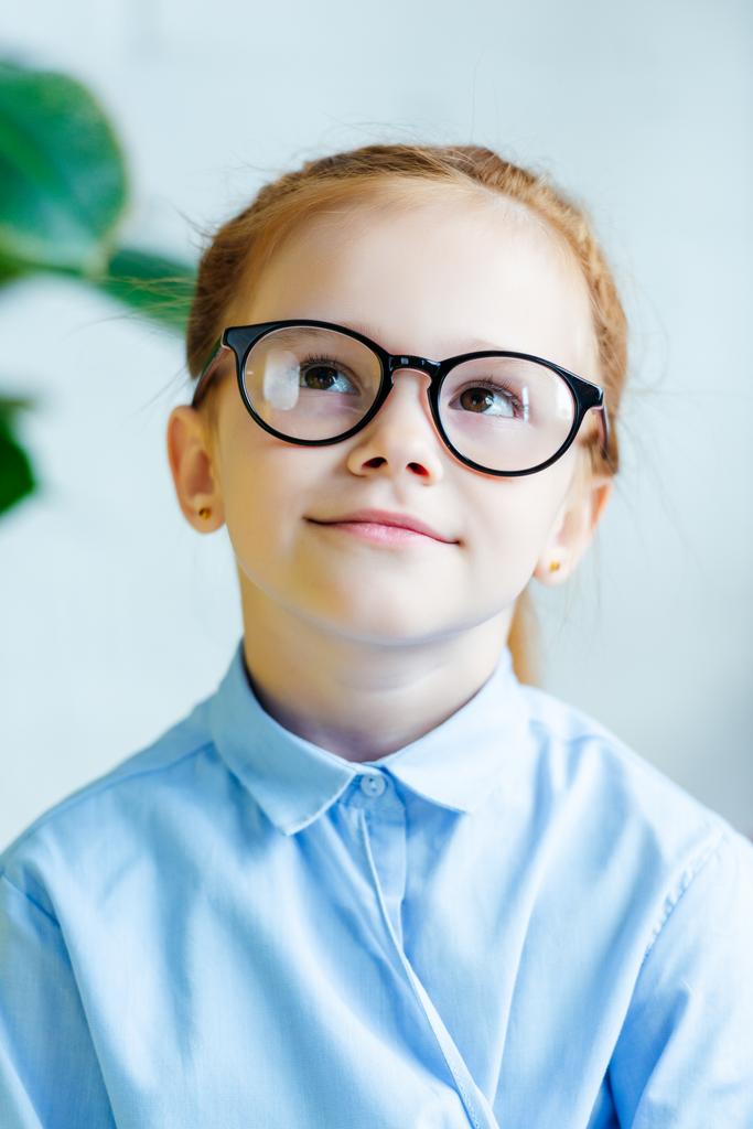 Porträt eines schönen kleinen rothaarigen Kindes mit Brille, das lächelt und nach oben schaut - Foto, Bild