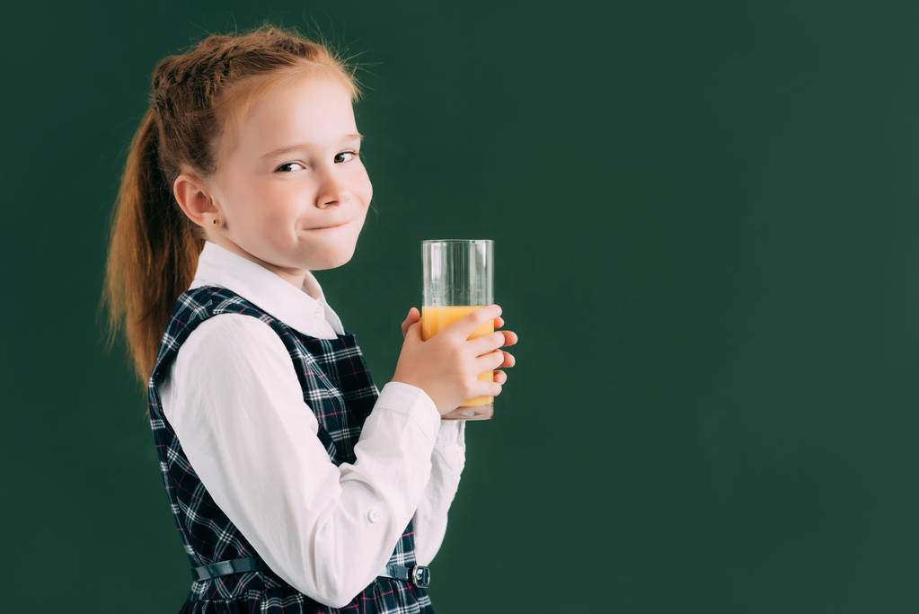 entzückendes kleines Schulmädchen hält ein Glas Orangensaft in der Hand und lächelt in die Kamera  - Foto, Bild