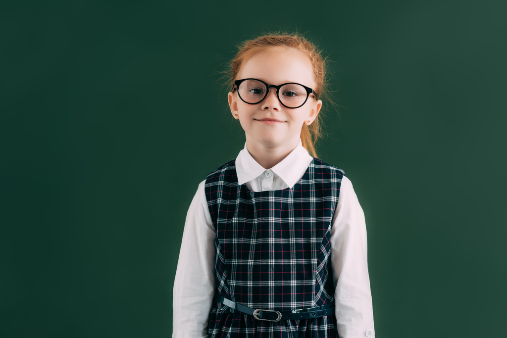 sevimli küçük kız öğrenci kara tahta duran ve kameraya gülümseyen gözlük - Fotoğraf, Görsel