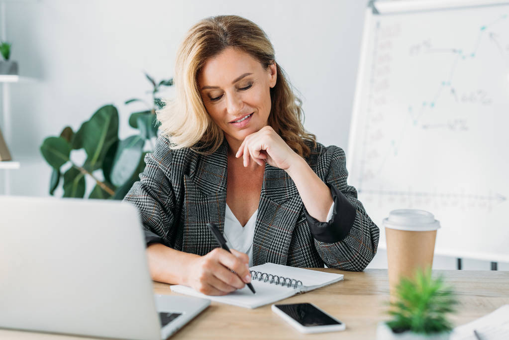 attractive businesswoman writing something to notebook in office - Photo, Image