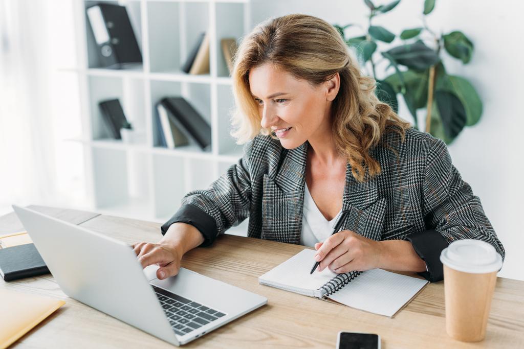 atractiva mujer de negocios que utiliza el ordenador portátil y escribir algo para portátil en la oficina
 - Foto, imagen