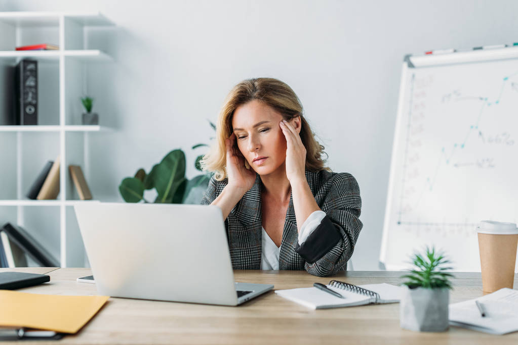 aantrekkelijke zakenvrouw met hoofdpijn en kijken naar laptop in kantoor - Foto, afbeelding