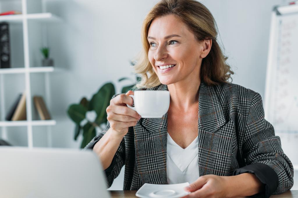 atrakcyjna kobieta siedząc z filiżanką kawy w tabeli w biurze i szukasz drogi - Zdjęcie, obraz