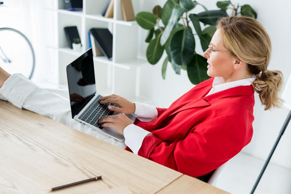 mulher de negócios atraente que trabalha com laptop e pernas na mesa no escritório
 - Foto, Imagem