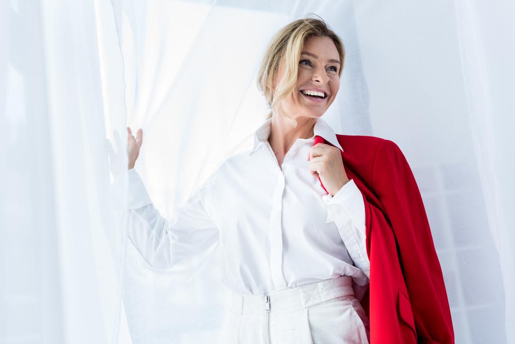 atractiva mujer de negocios sosteniendo chaqueta roja y mirando hacia otro lado en la oficina
 - Foto, imagen