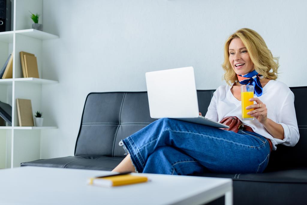 привлекательная деловая женщина работает с ноутбуком в офисе и держит стакан сока
 - Фото, изображение