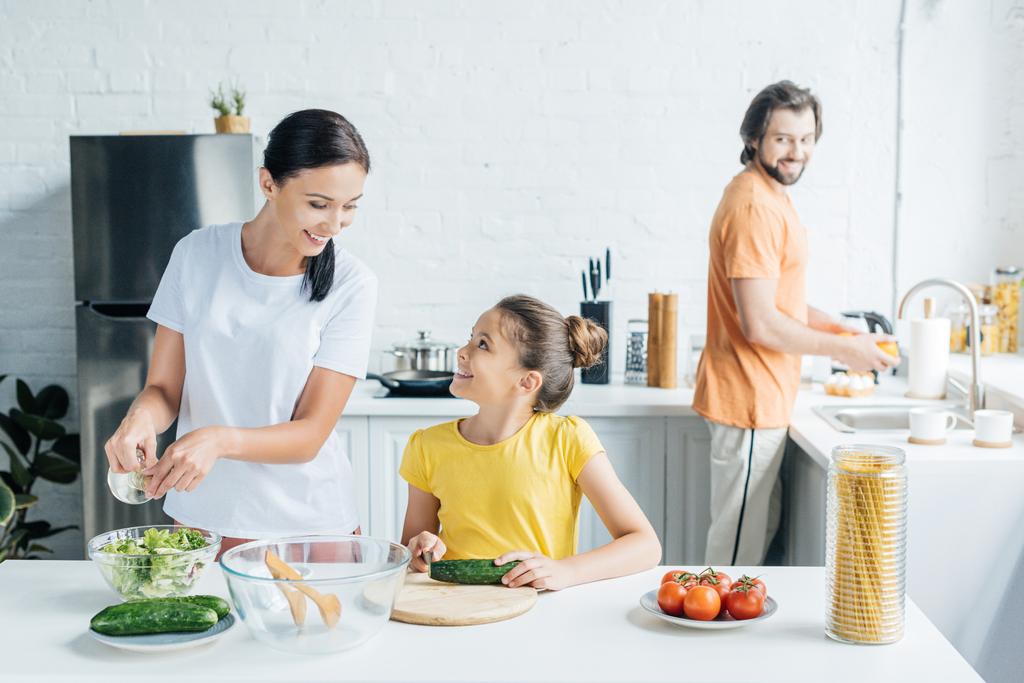 anya és lánya, saláta, míg apja a háttérben, konyhai mosogatás előkészítése - Fotó, kép