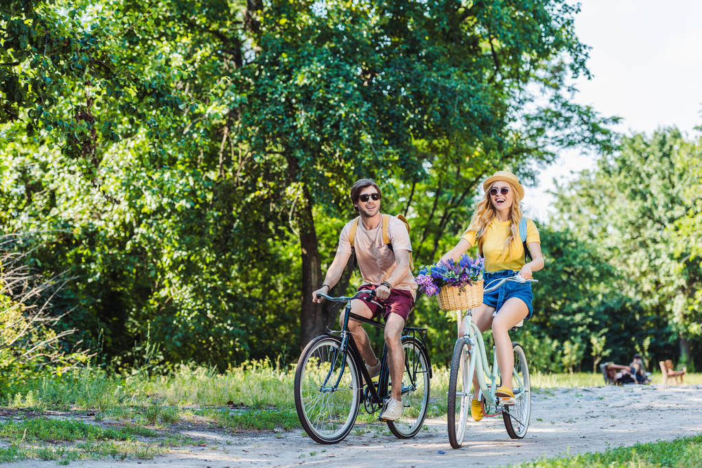 young happy couple riding retro bicycles in park on summer day - Photo, Image