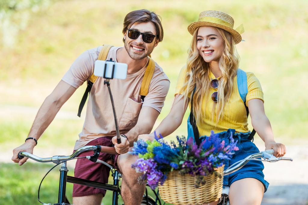 Улыбающаяся пара влюблена в велосипеды, делающие селфи в парке в летний день
 - Фото, изображение