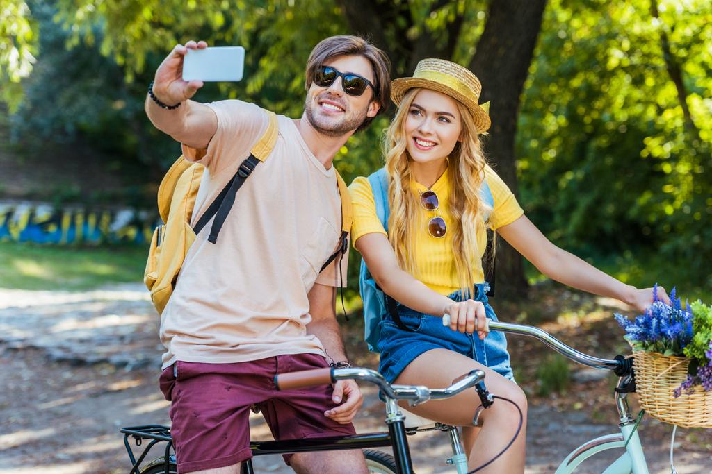 coppia sorridente innamorata delle biciclette scattando selfie nel parco nella giornata estiva
 - Foto, immagini