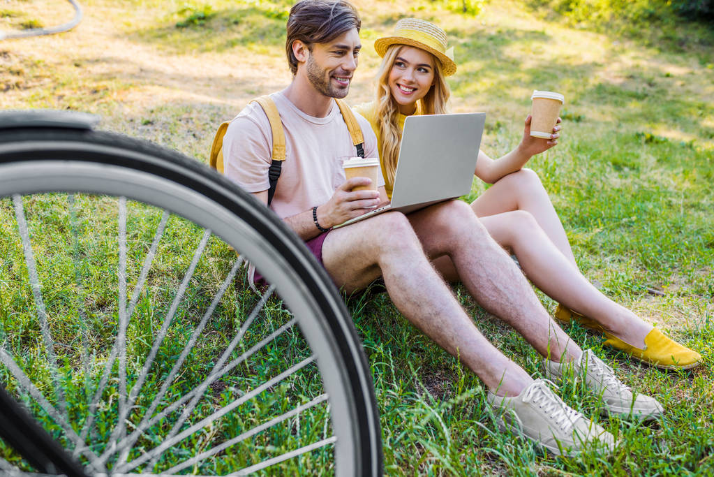 young couple with coffee to go using laptop in park - Photo, Image