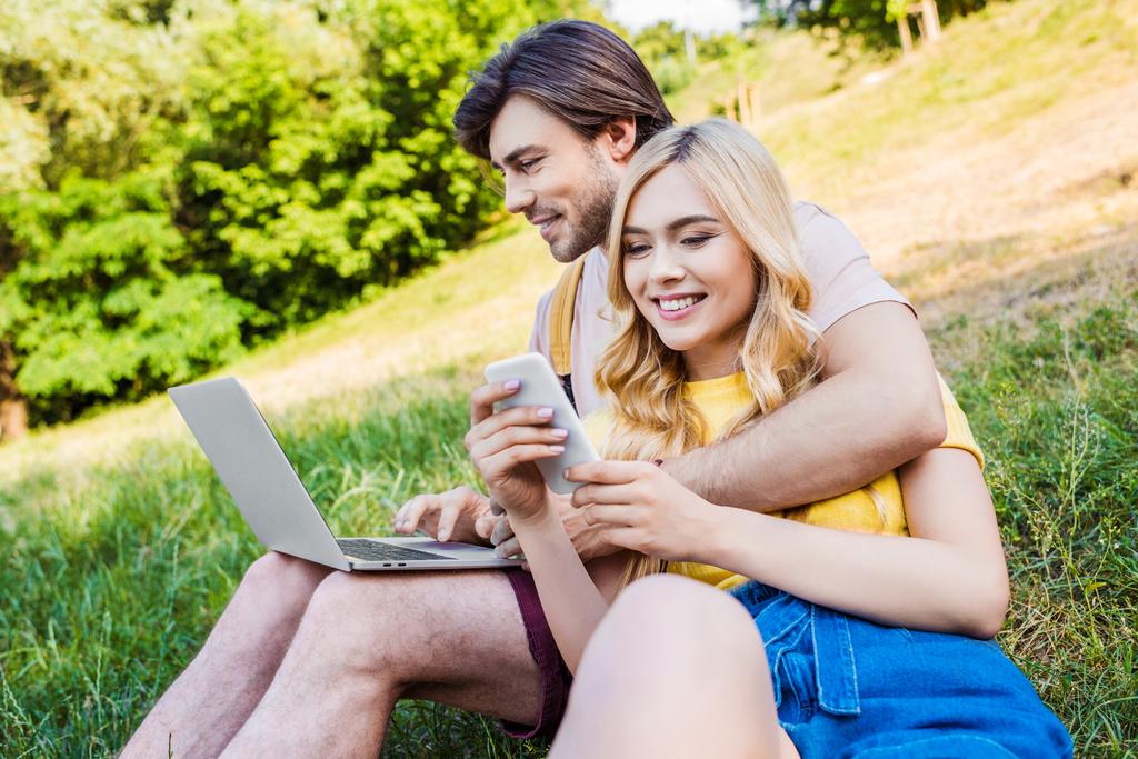 νεαρό ζευγάρι με laptop και smartphone που ακουμπά σε πράσινο γρασίδι στο πάρκο - Φωτογραφία, εικόνα