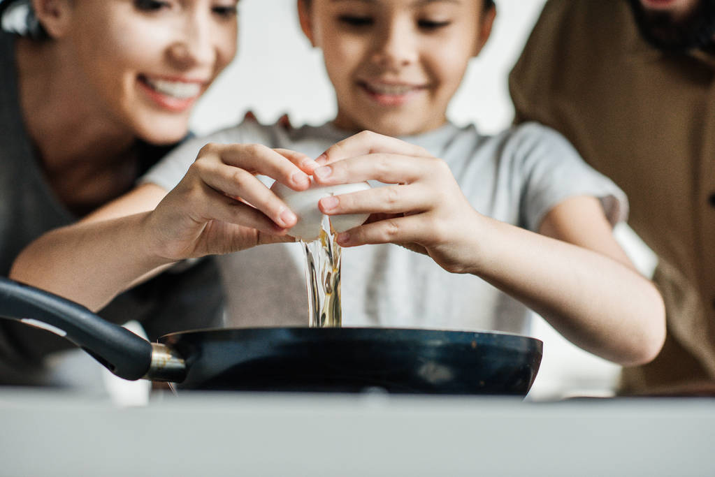 zbliżenie dziewczynka łamanie jajko na patelni podczas gotowania z rodzicami - Zdjęcie, obraz