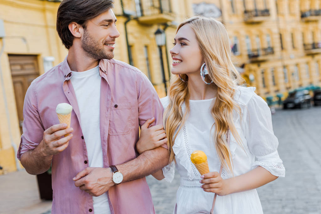Porträt eines jungen Paares mit Eis, das an einem Sommertag auf der Straße spaziert - Foto, Bild