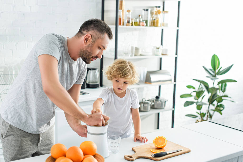padre e piccolo figlio facendo succo d'arancia fresco da spremiagrumi sul tavolo in cucina figlio
  - Foto, immagini