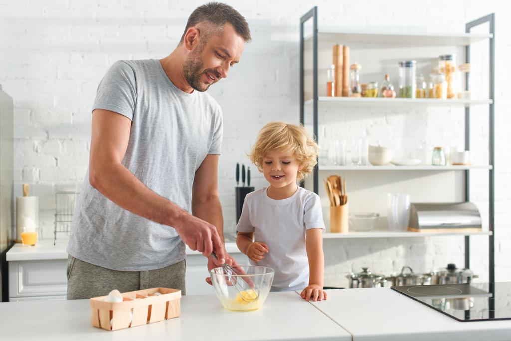 pai e filho batendo ovos na tigela na mesa na cozinha
  - Foto, Imagem