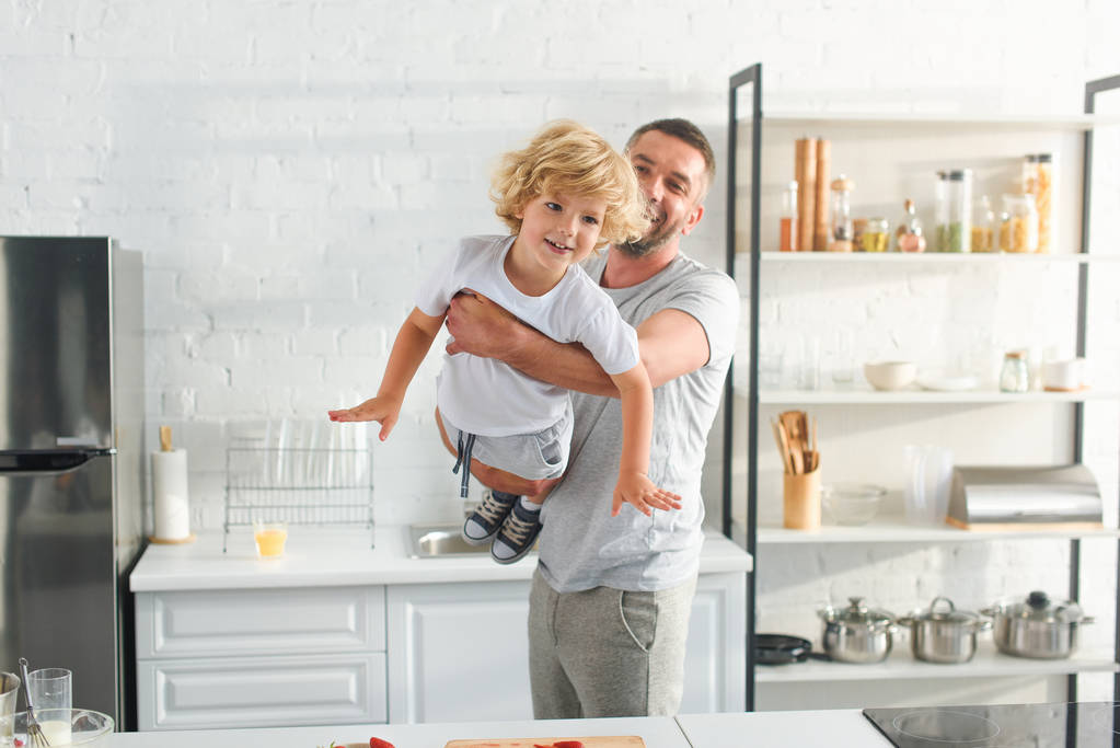 padre levantando sonriente pequeño hijo en la cocina
 - Foto, Imagen