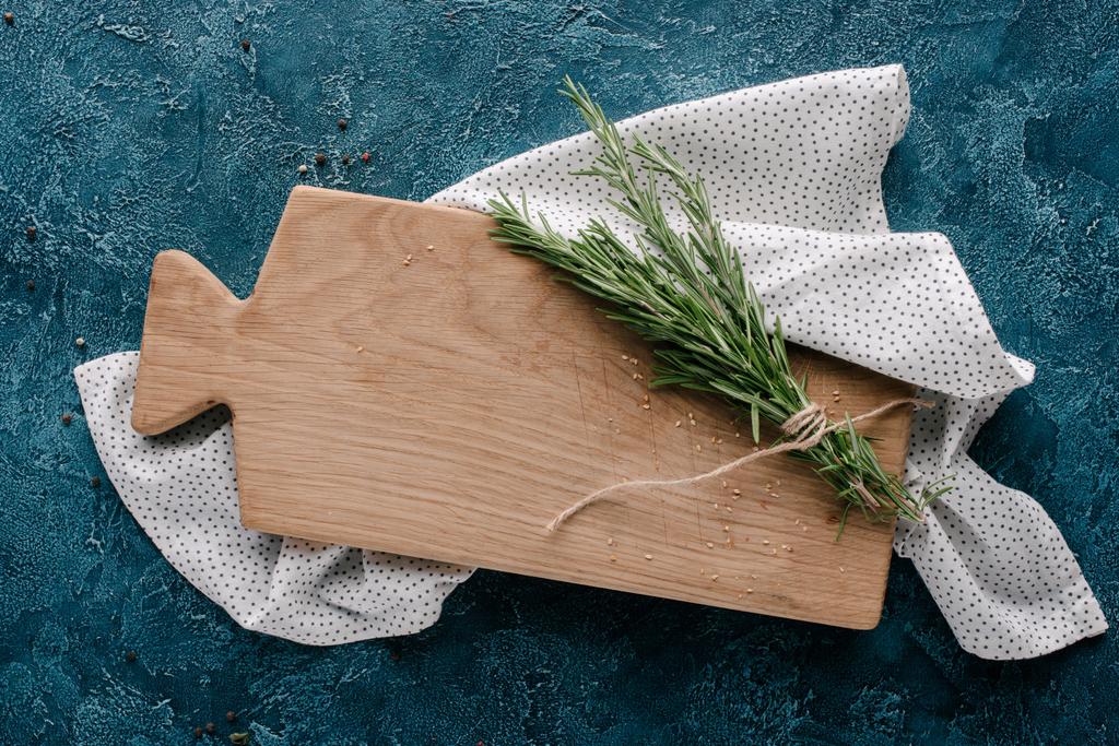 Tagliere in legno con erba di rosmarino su tavolo blu scuro
 - Foto, immagini