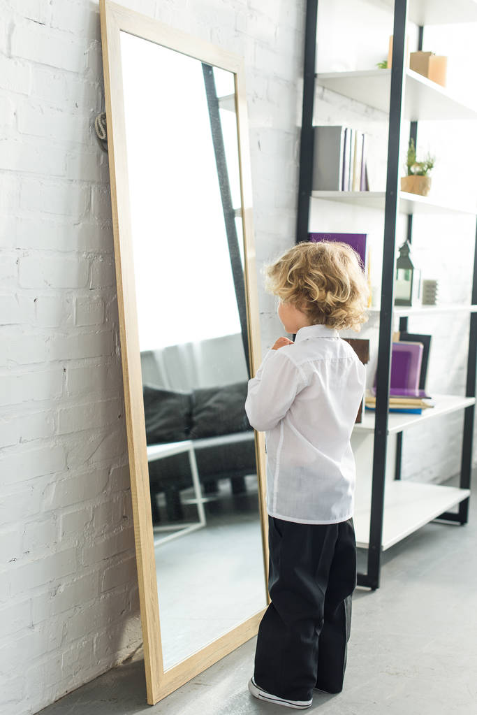 自宅の鏡の前で白いシャツの上にネクタイを結ぶ小さな男の子の背面図  - 写真・画像