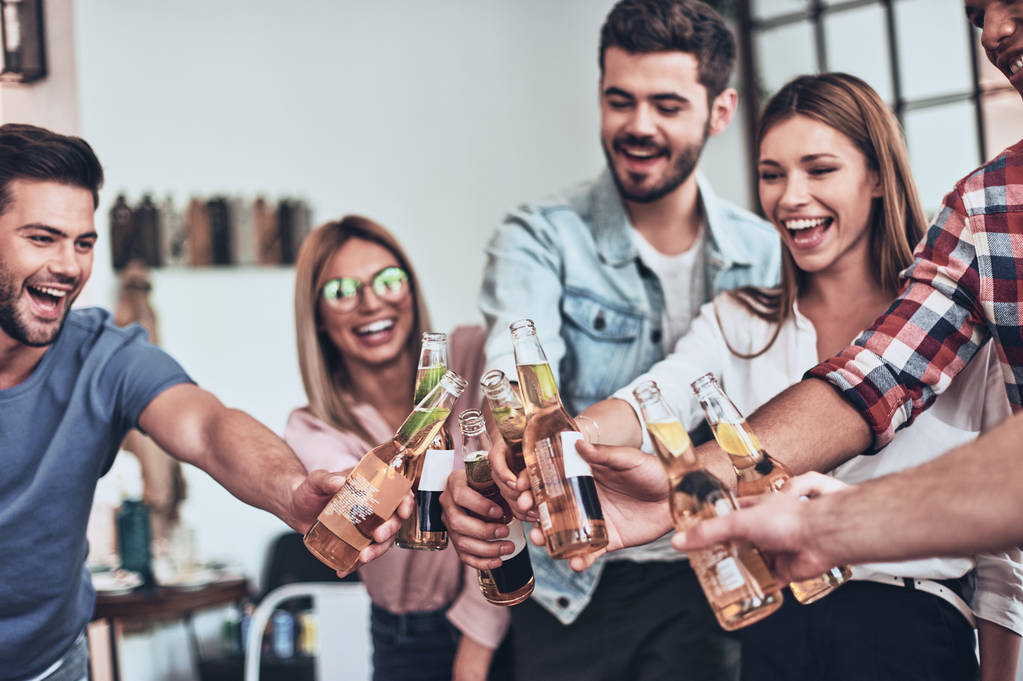 elegantes amigos brindando entre sí con botellas de cerveza mientras tienen fiesta en el interior
 - Foto, Imagen