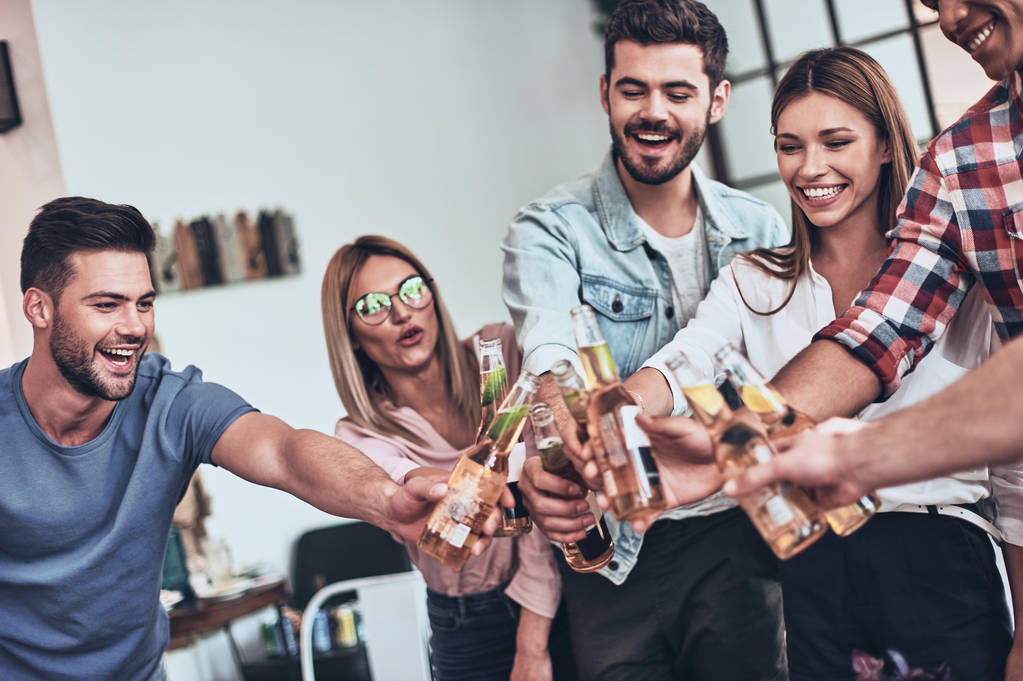stilvolle Freunde, die sich mit Bierflaschen anstoßen, während sie drinnen feiern - Foto, Bild