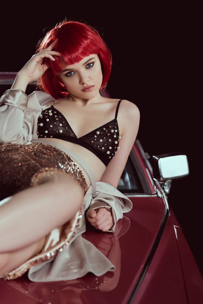 красивая молодая женщина в бюстгальтере и стильном плаще смотрит в камеру, когда лежит на машине
    - Фото, изображение