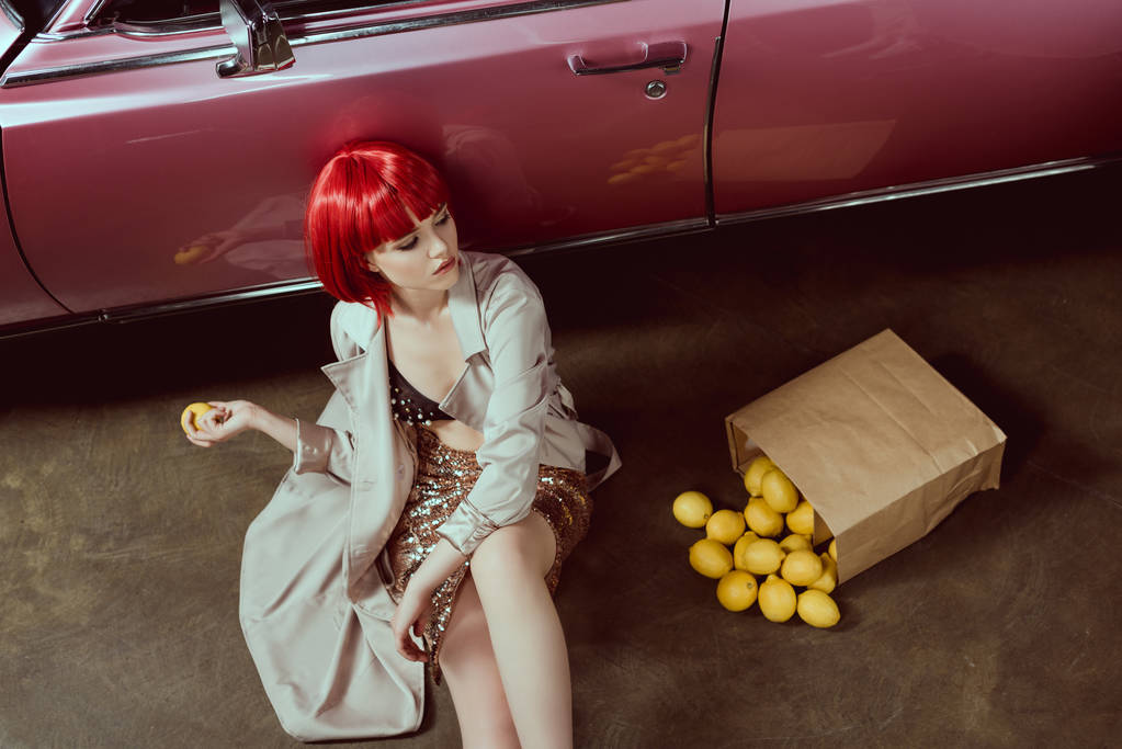 korkea kulma näkymä kaunis tyttö tyylikäs trench takki tilalla sitruuna istuessaan lähellä retro auto
  - Valokuva, kuva
