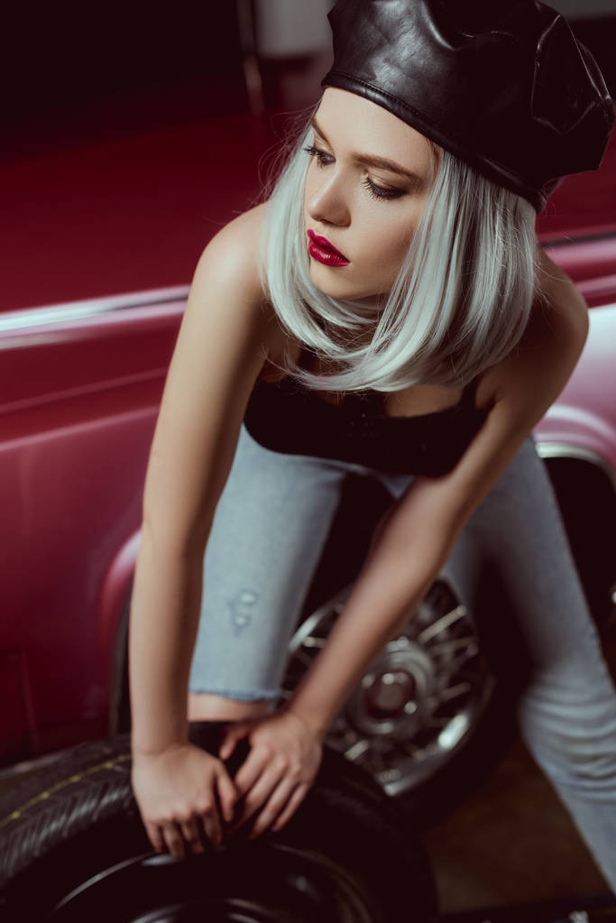 beautiful young blonde woman in leather beret repairing car and looking away - Photo, Image