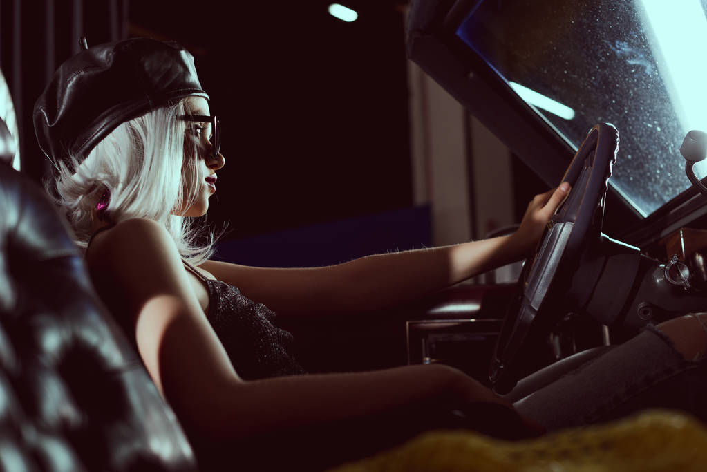 side view of beautiful young blonde woman in beret driving retro car - Photo, Image