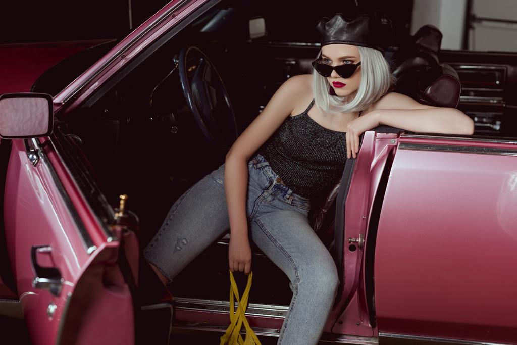 wysoki kąt widzenia stylowa dziewczyna Blondynka w beret i okulary przeciwsłoneczne, trzymając worek ciąg siedząc w samochodzie  - Zdjęcie, obraz