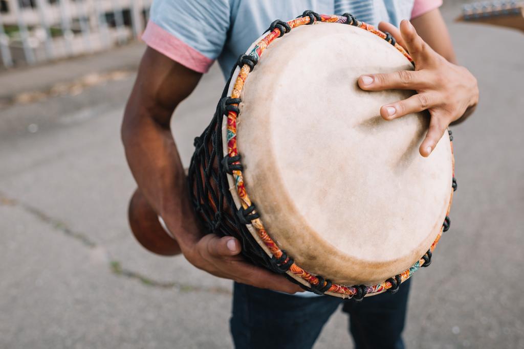 Vista recortada del músico callejero afroamericano tocando djembe en la ciudad
 - Foto, Imagen