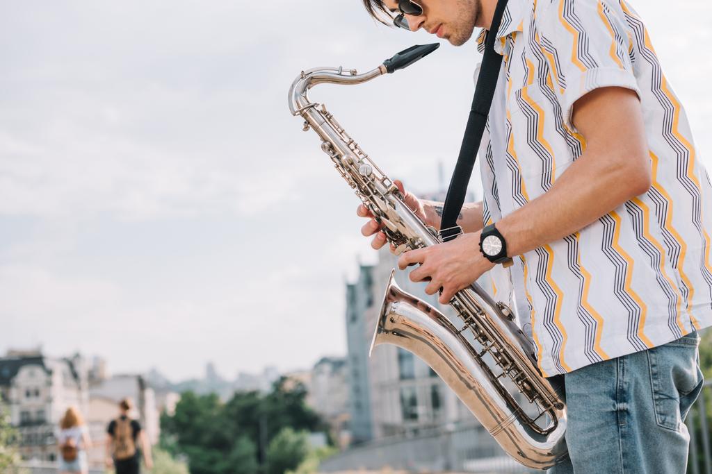 Jovem hipster homem com saxofone se apresentando na rua
 - Foto, Imagem