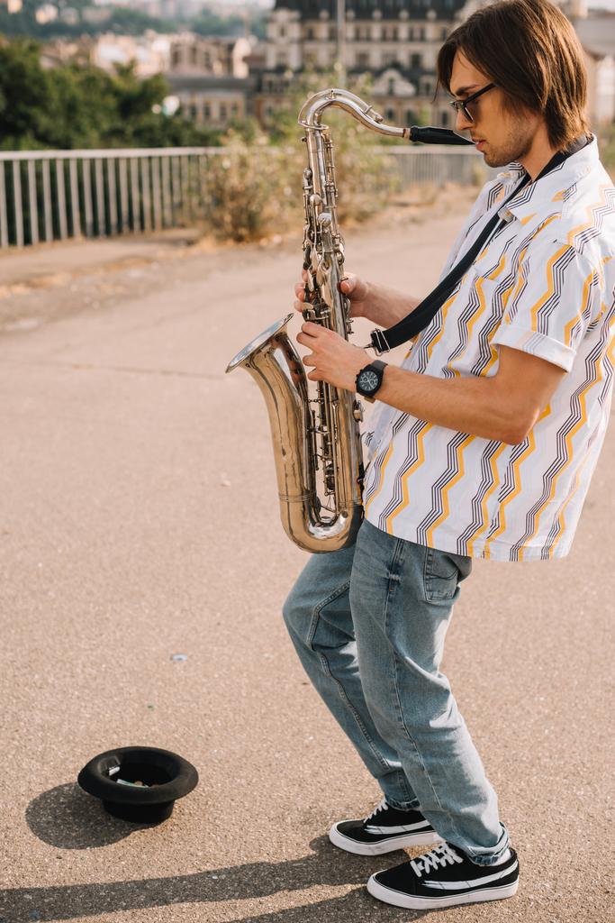 Молодой человек с саксофоном выступает в городской среде
 - Фото, изображение