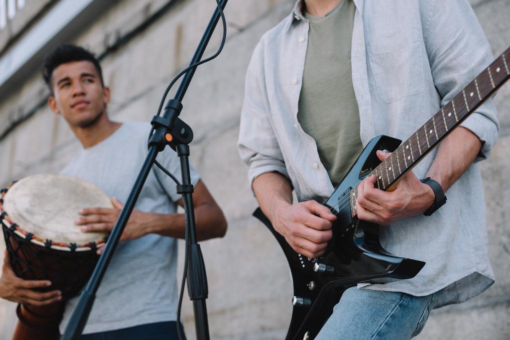 Junge fröhliche männliche Straßenmusiker spielen Gitarre und Djembe in der City Street - Foto, Bild