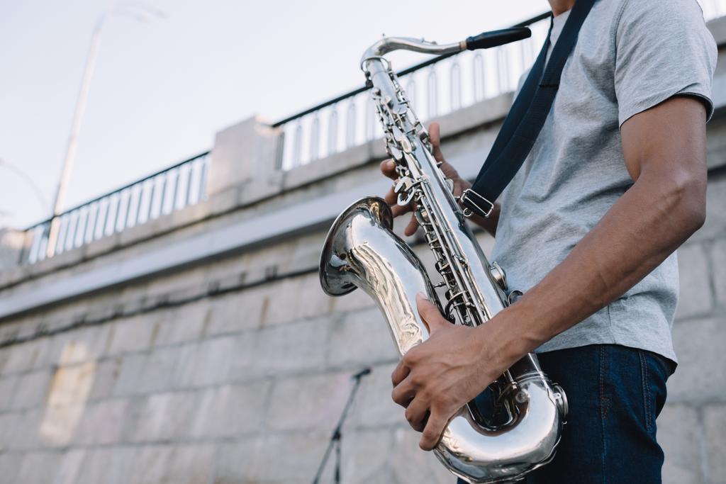 Cropped view of african american man playing saxophone performing on sunny city street - Photo, Image