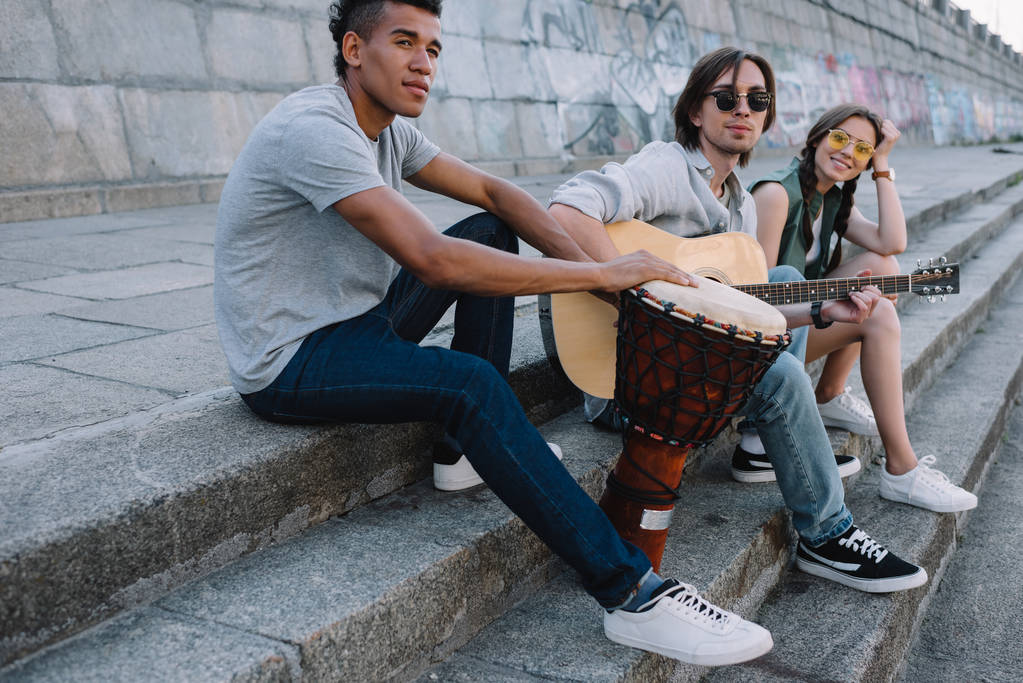 Jeune et heureux groupe de musiciens de rue multiraciaux assis avec des instruments en ville
 - Photo, image