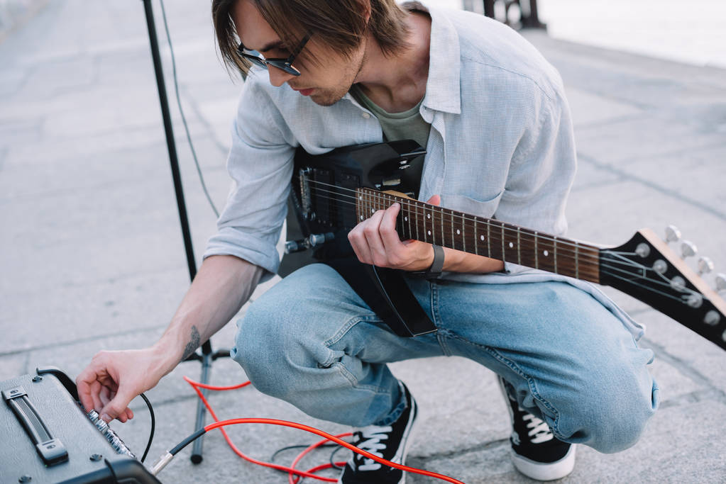 Jovem homem ajustando amplificador de guitarra enquanto se apresenta na rua
 - Foto, Imagem