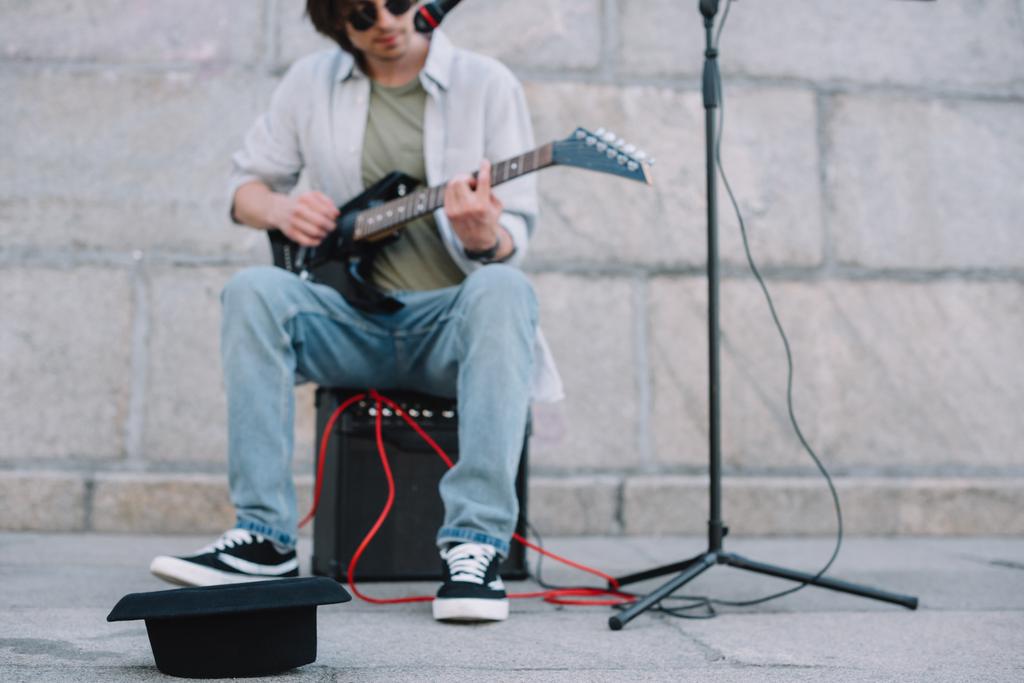 Chapéu vazio na frente do busker tocando guitarra e cantando em ambiente urbano - Foto, Imagem